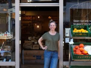 Ramona Schalkwijk staat lachend in de deuropening van boerenwinkel Oogst, naast kratten met groente en fruit