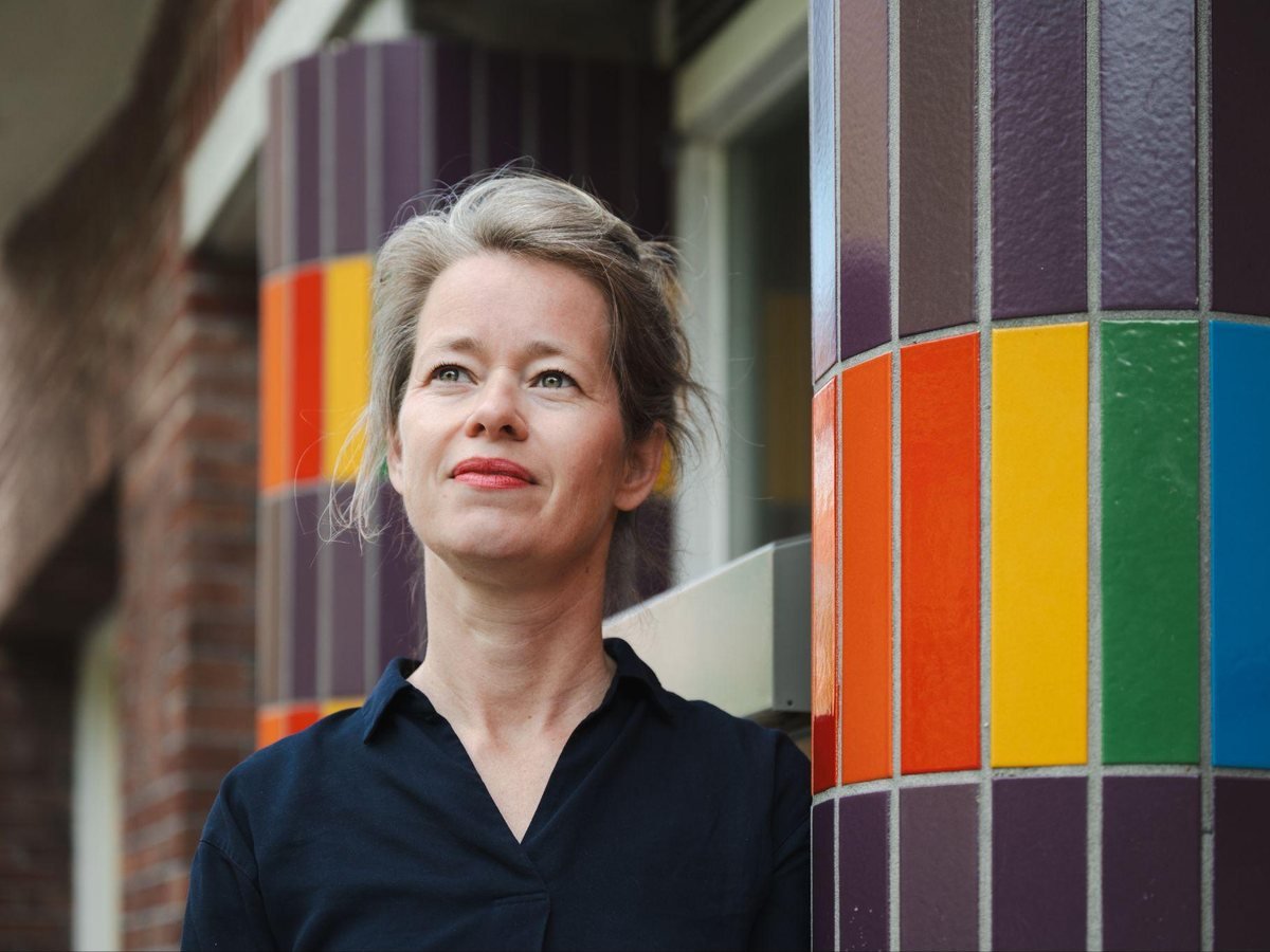 Willemijn Vermeer leunt tegen een gekleurde tegelzuil en kijkt omhoog